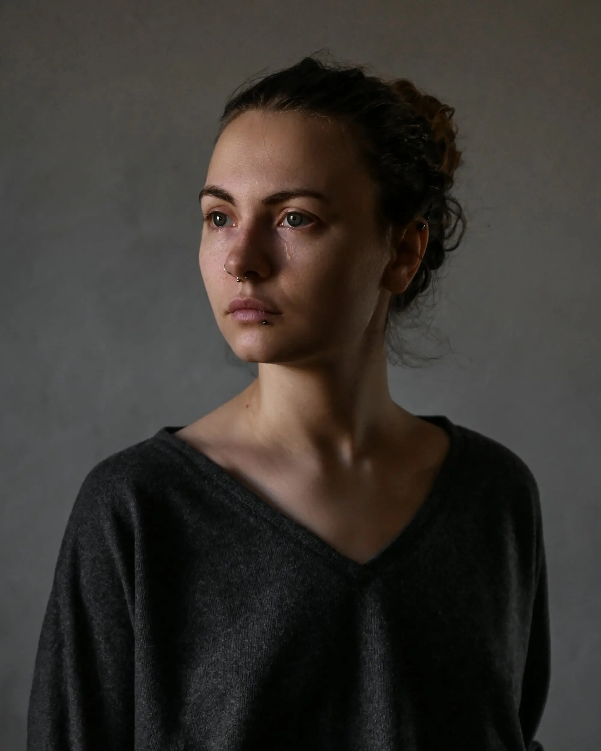 Portrait of a person with dark hair tied back, in muted light