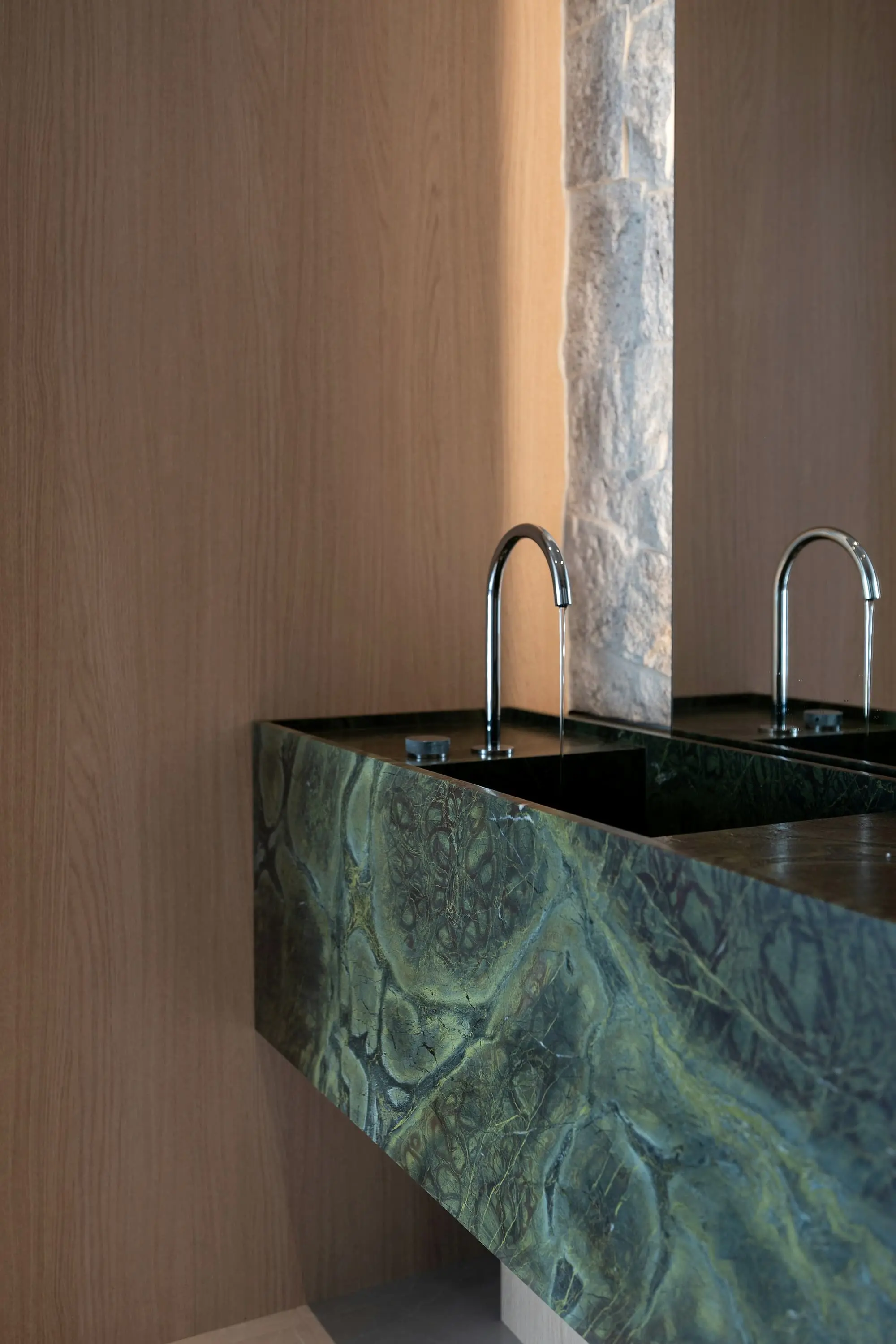 Bathroom basin carved from green marble with twin chrome taps against oak panelling