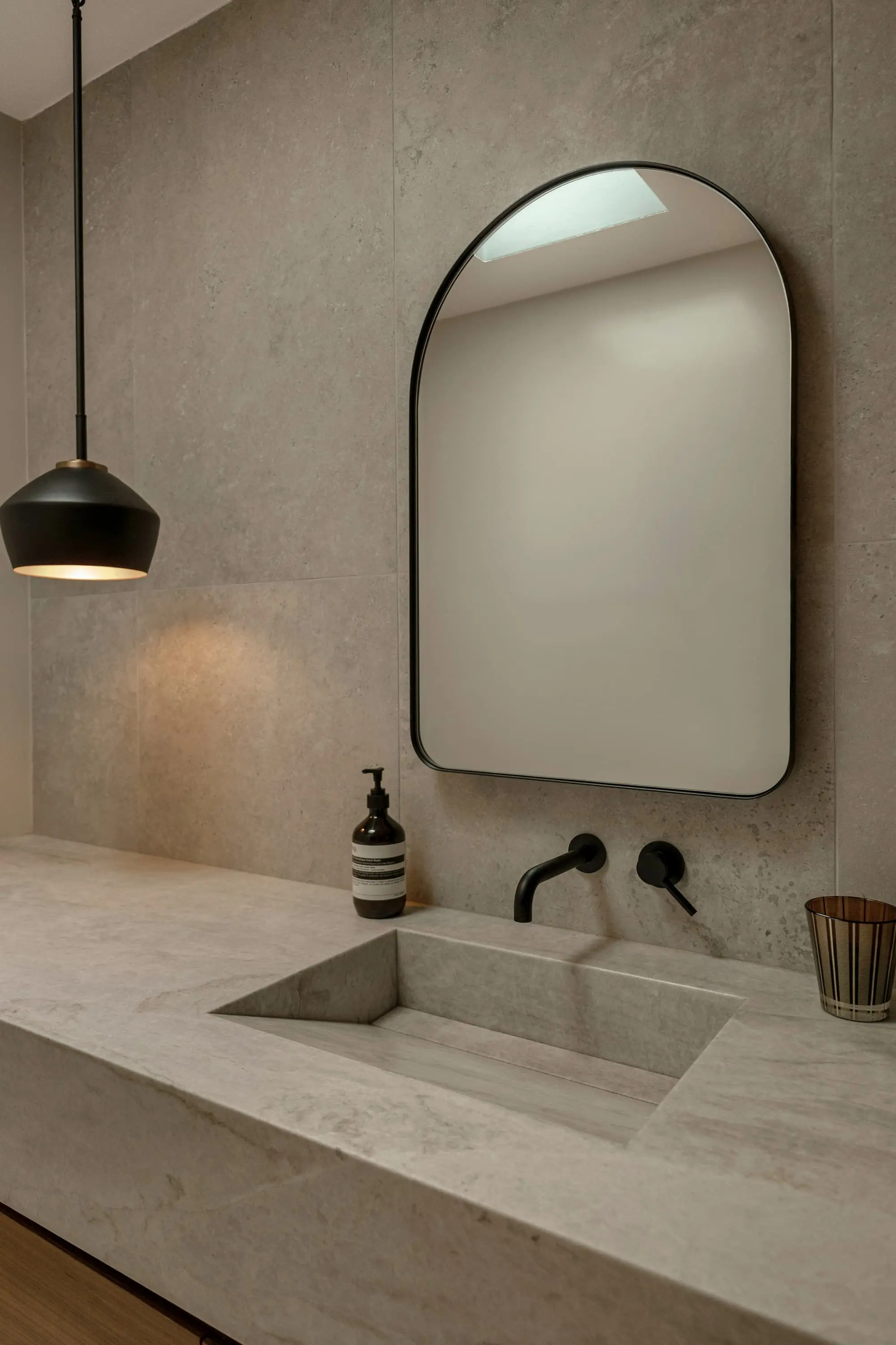 Bathroom with an arched mirror, a black wall tap and a pendant lamp over a stone basin