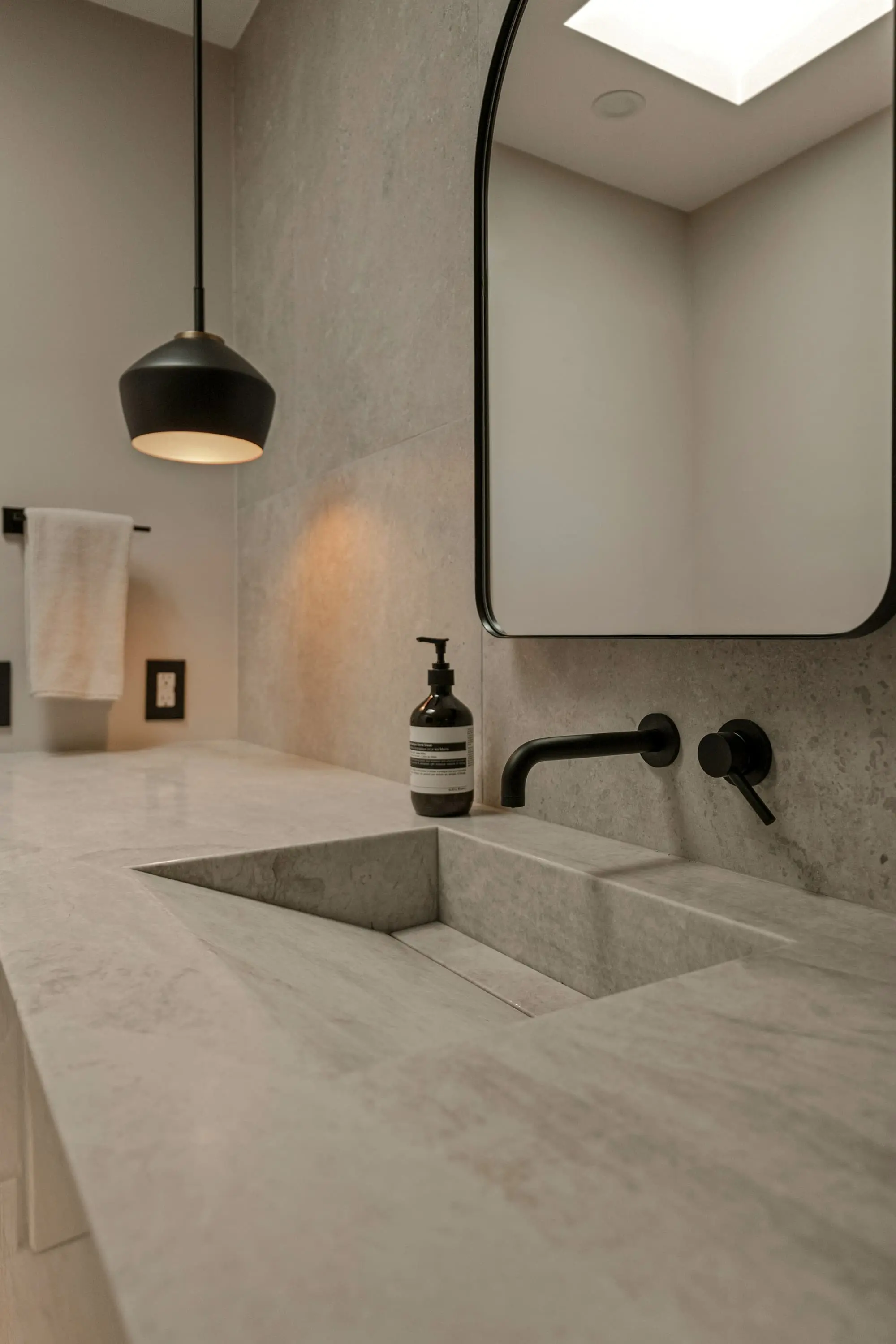 Honed stone basin with a wall-mounted black tap and a framed mirror