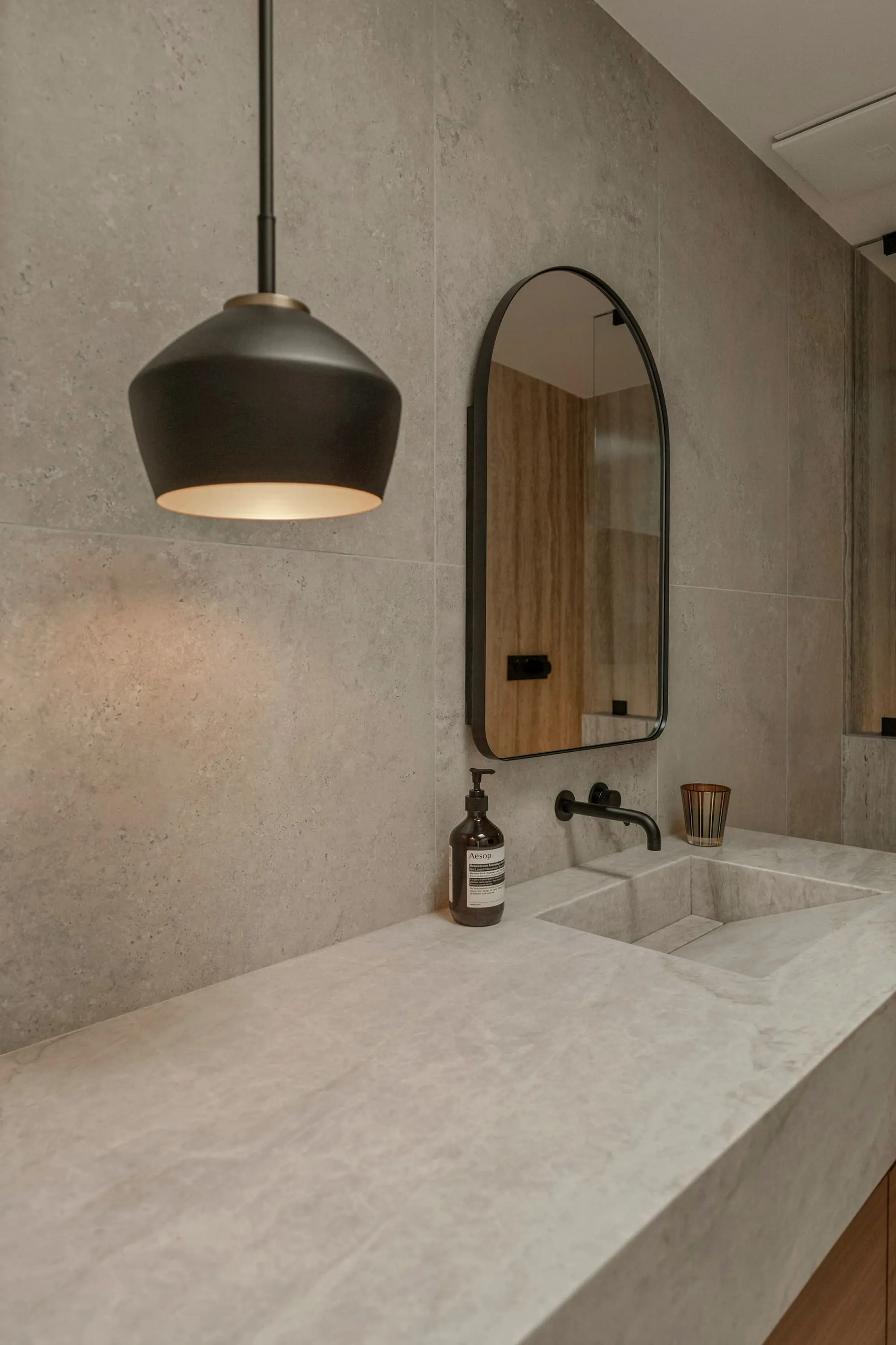 Bathroom vanity with a tall arched mirror, a black pendant and oak cabinet