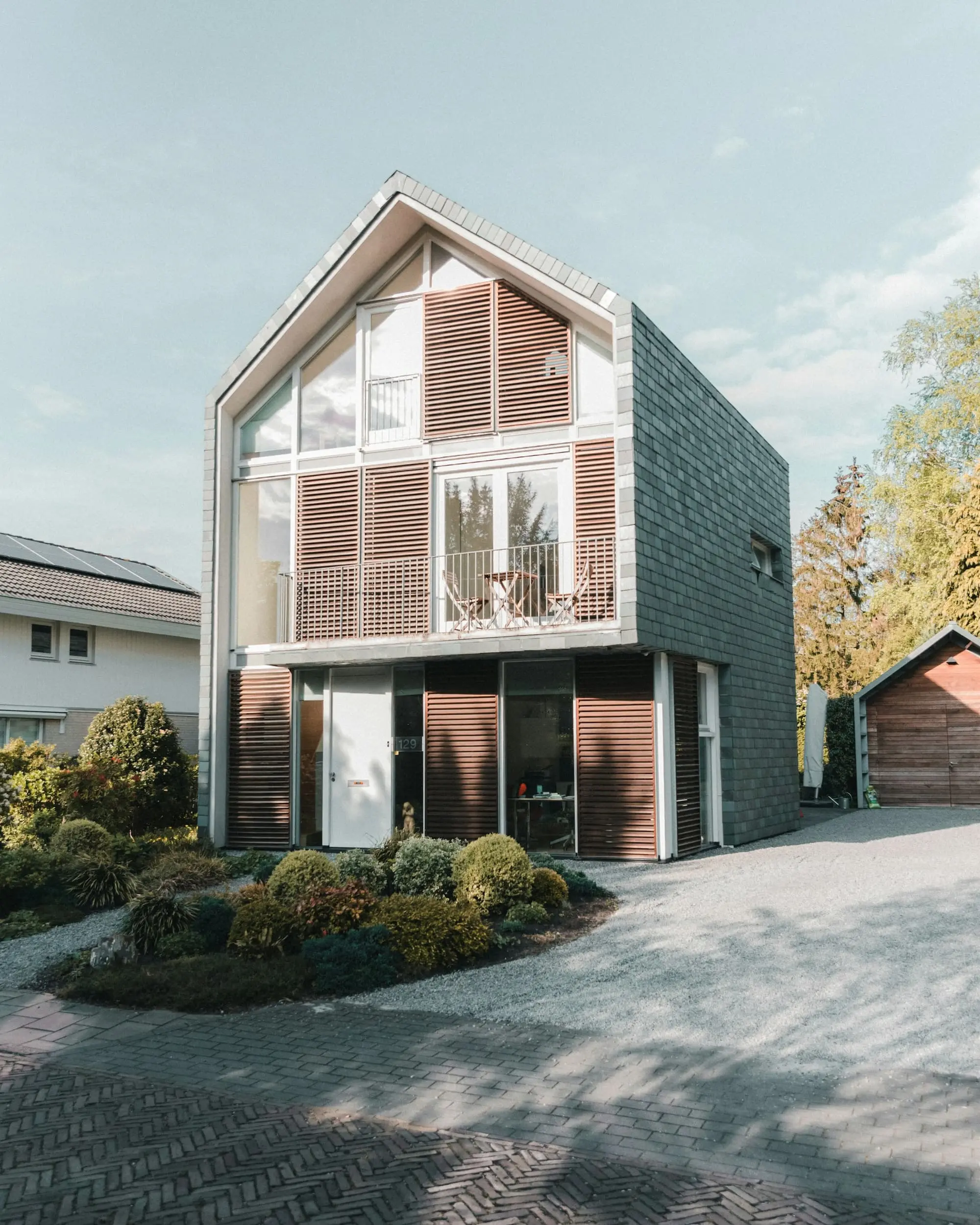 Narrow gabled townhouse clad in slate and timber louvres with a glazed upper floor