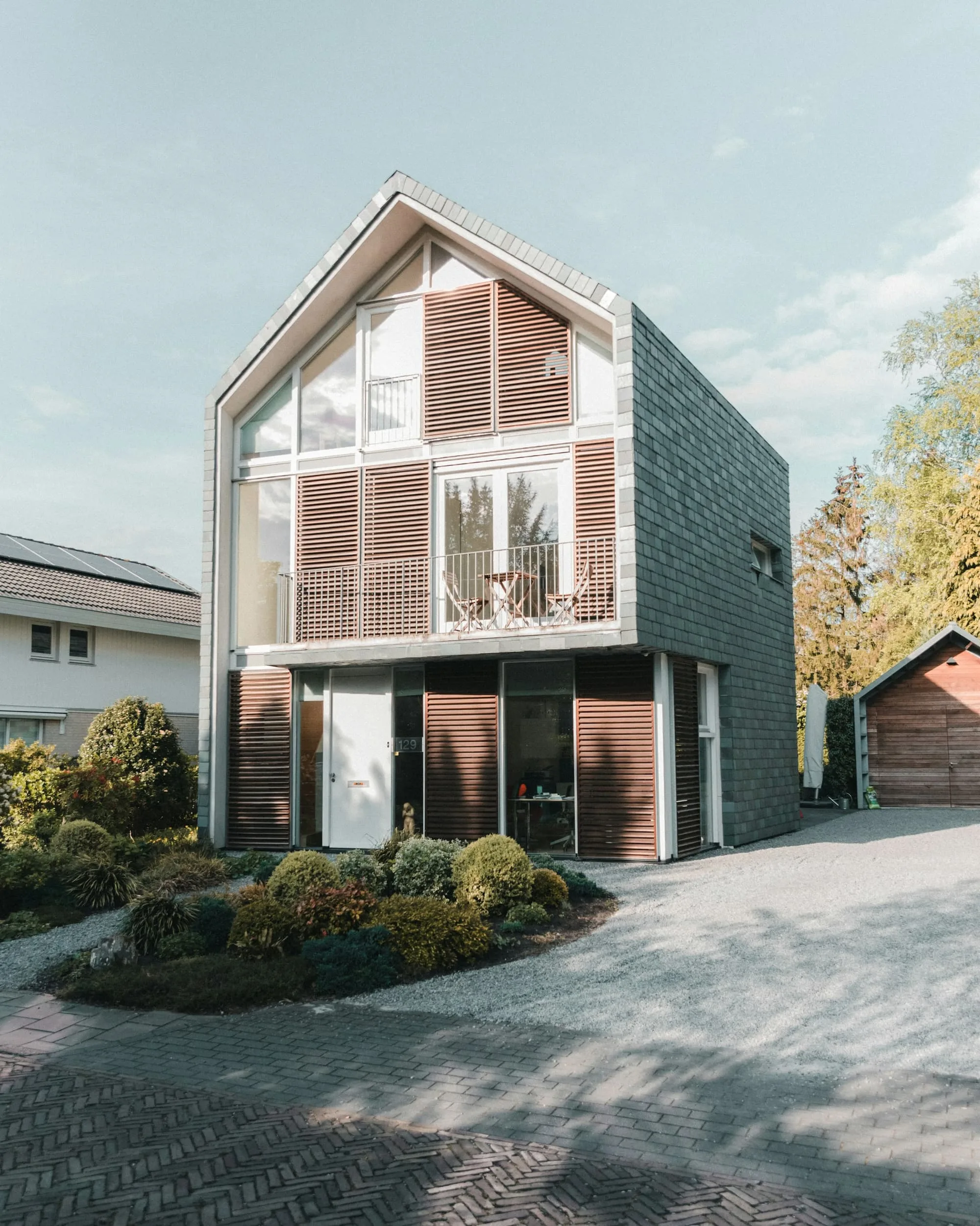 Narrow gabled townhouse clad in slate and timber louvres with a glazed upper floor