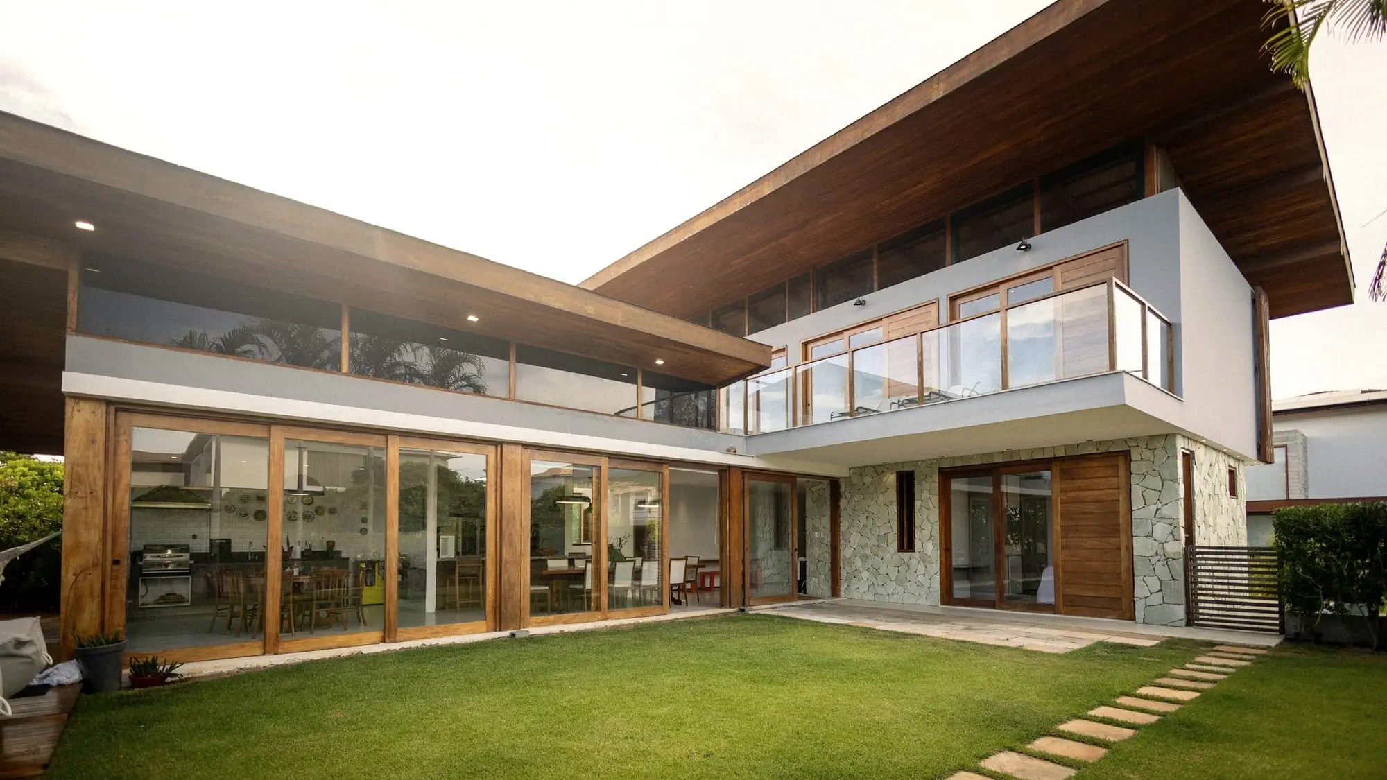 Two-storey contemporary villa with a deep timber roof overhang, glazed ground floor and a lawn in front