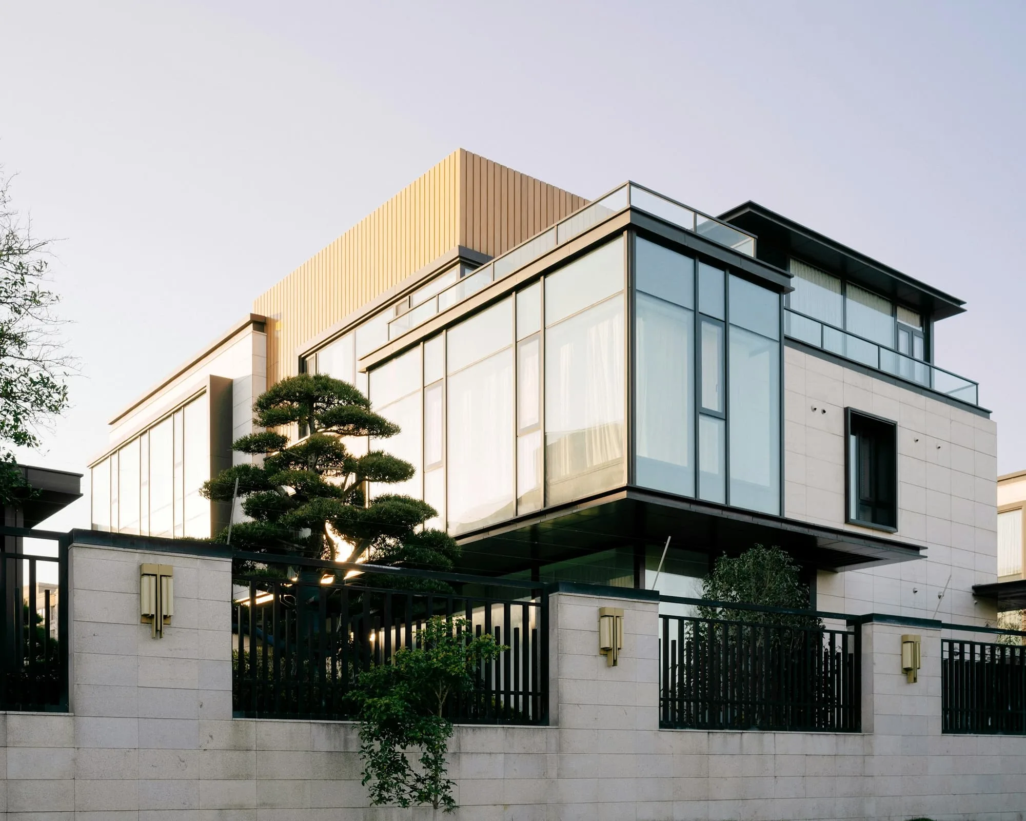Contemporary house with glazed corners and pale stone panels behind a garden wall