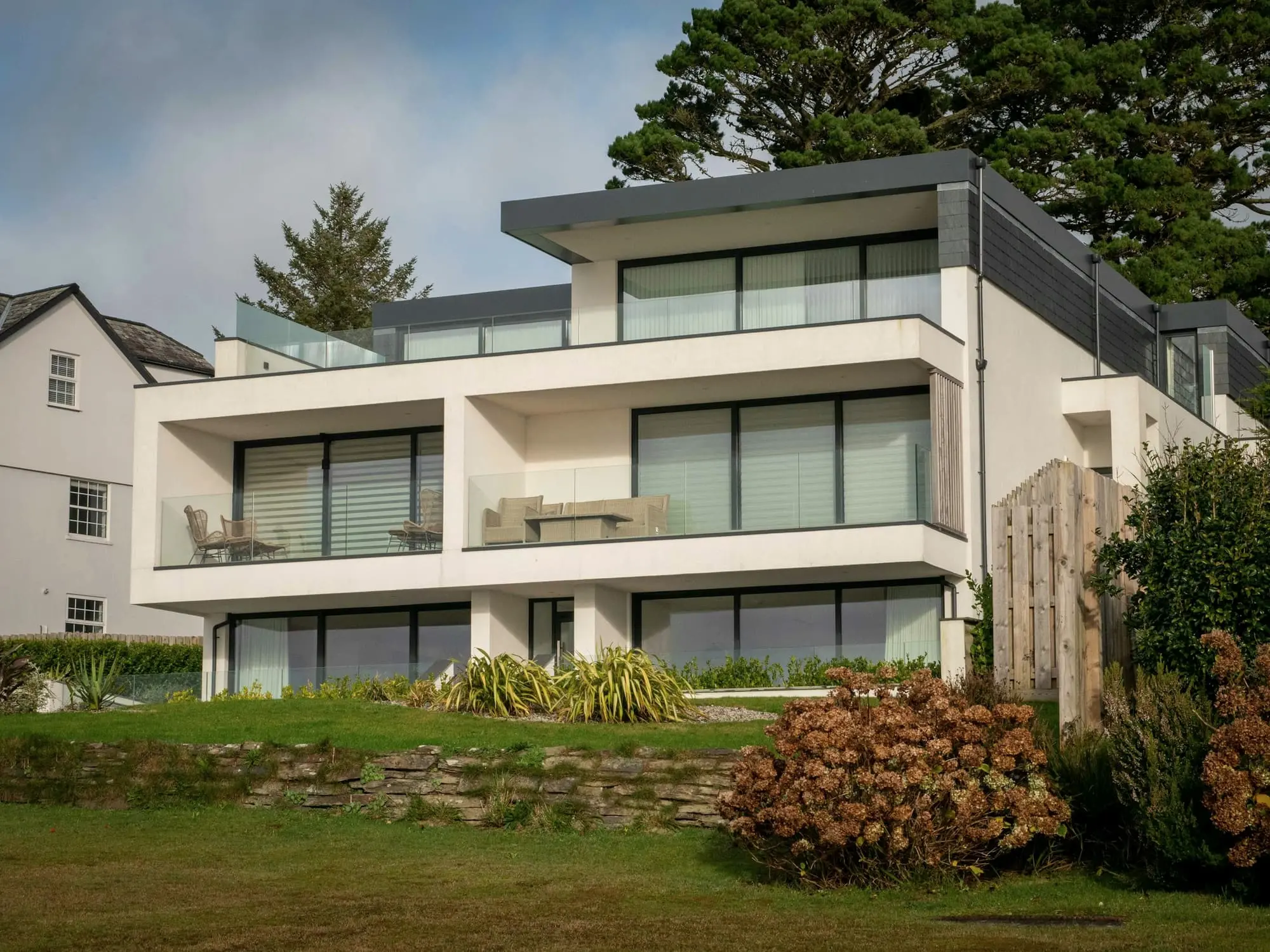 White three-level coastal house with terraces and glass balustrades above a lawn