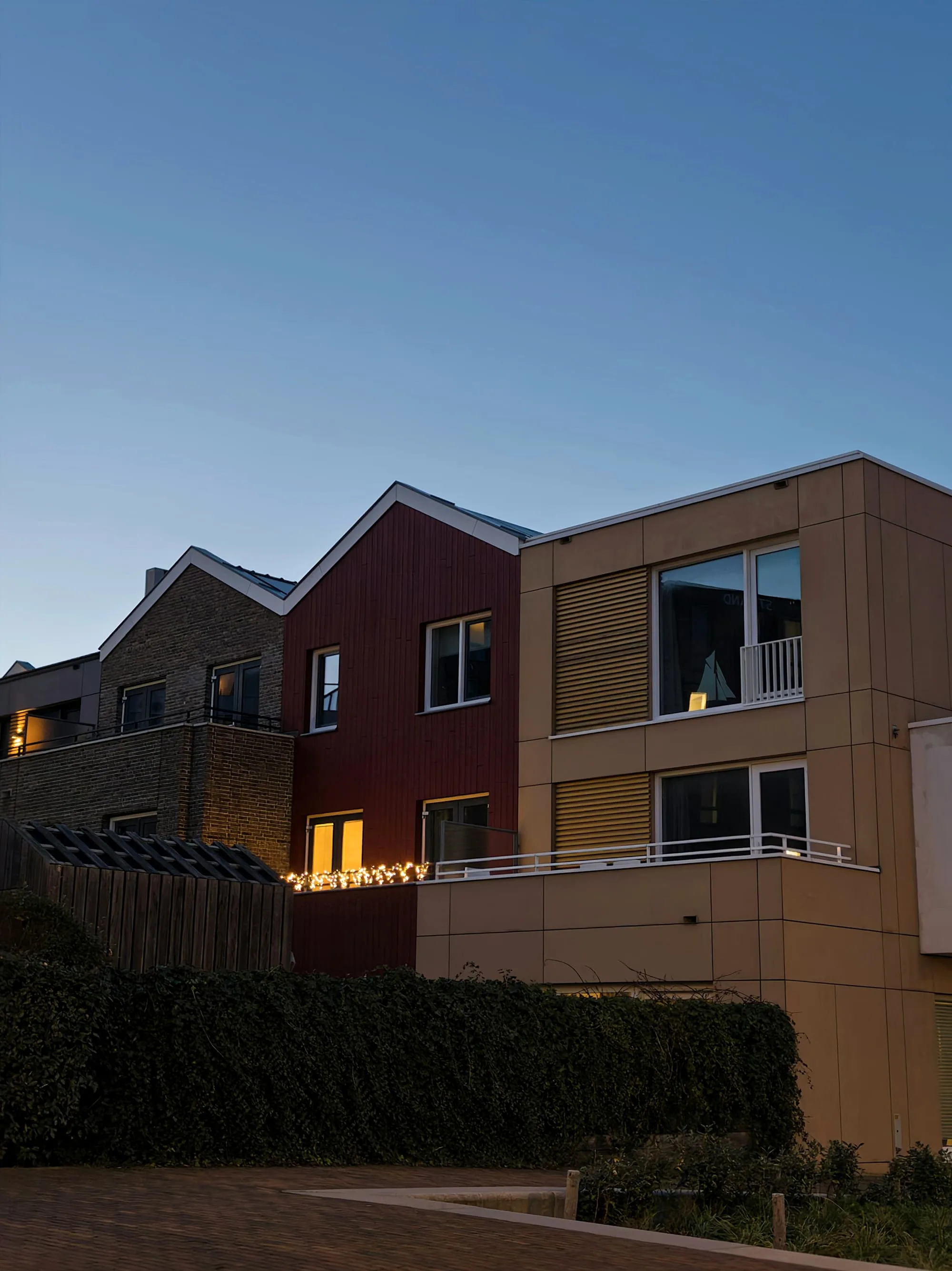 Terrace of gabled houses in timber and brick cladding, lit at dusk