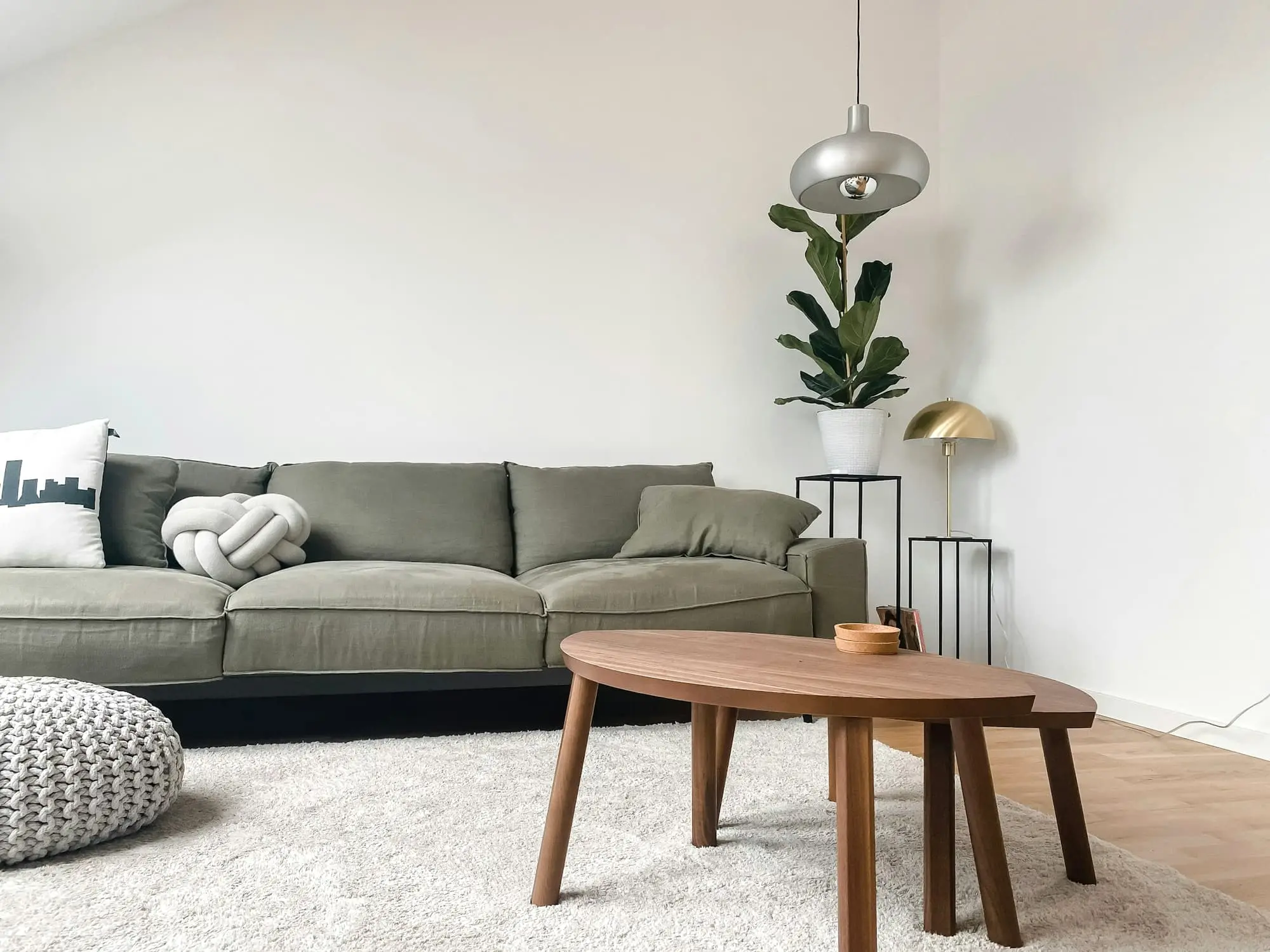 Sage sofa, curved walnut coffee table and a floor lamp in a white room
