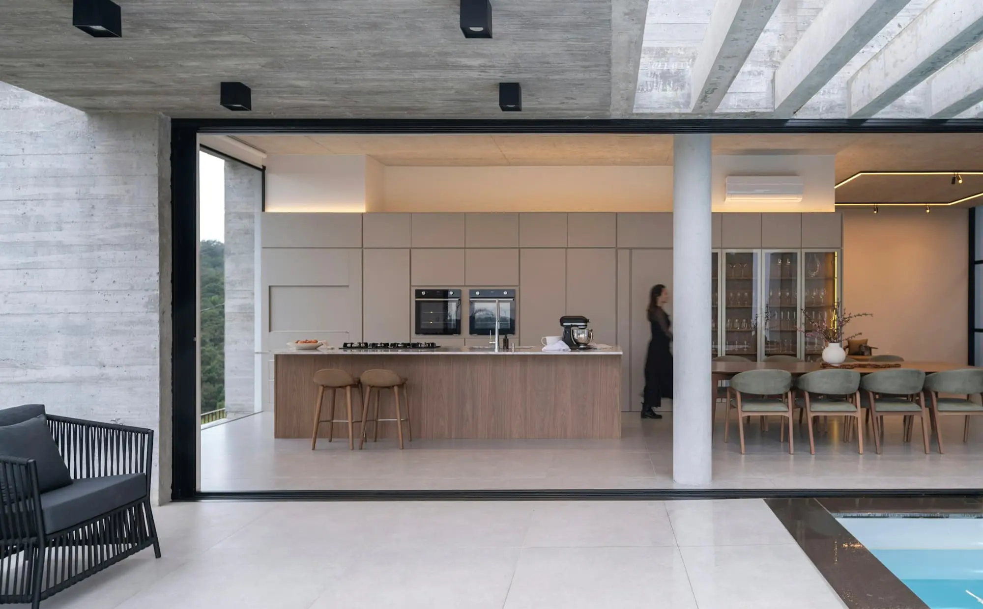 Long kitchen with a stone island, board-marked concrete ceiling and a dining table beyond