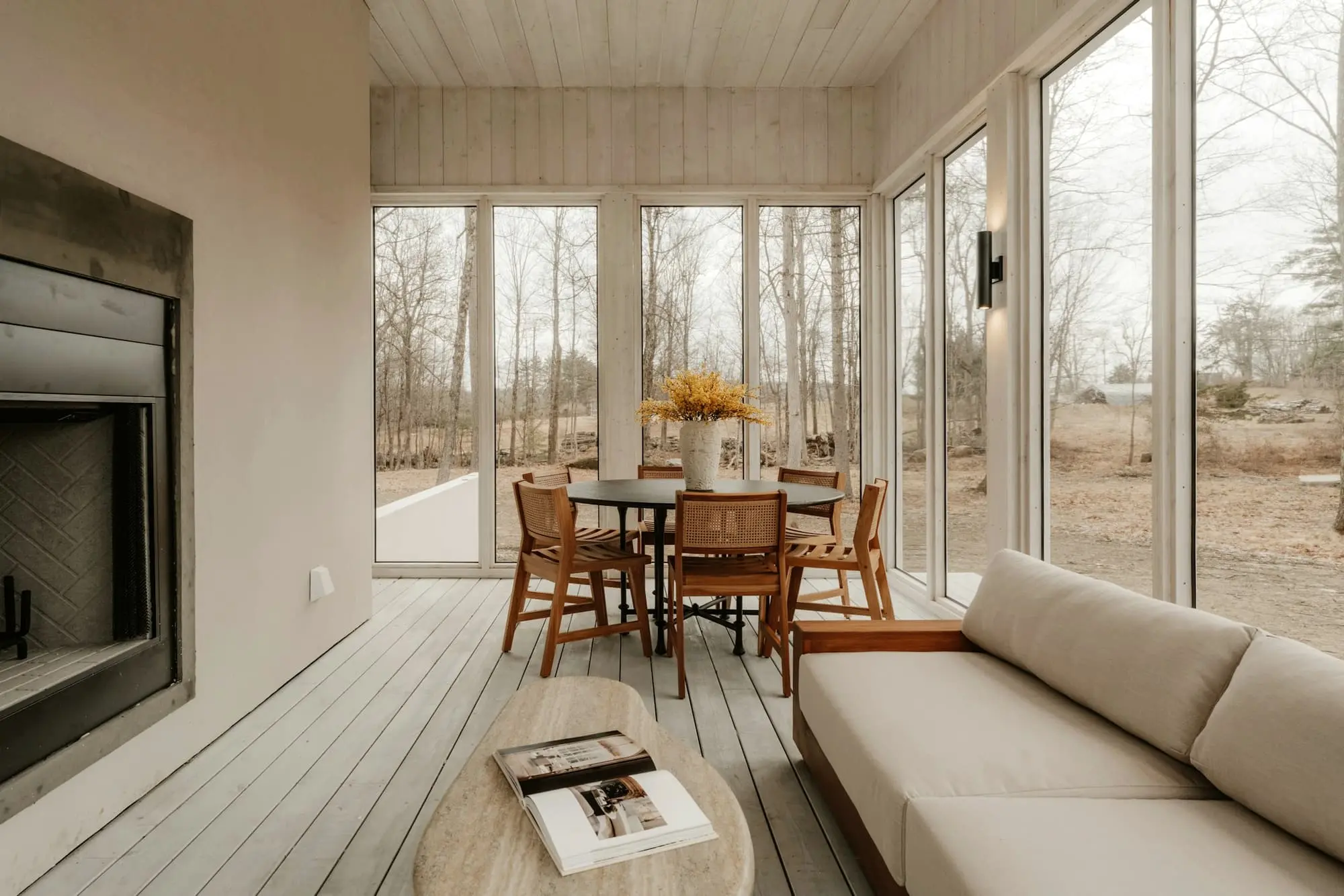 Dining and living area with floor-to-ceiling windows, a fireplace and timber chairs