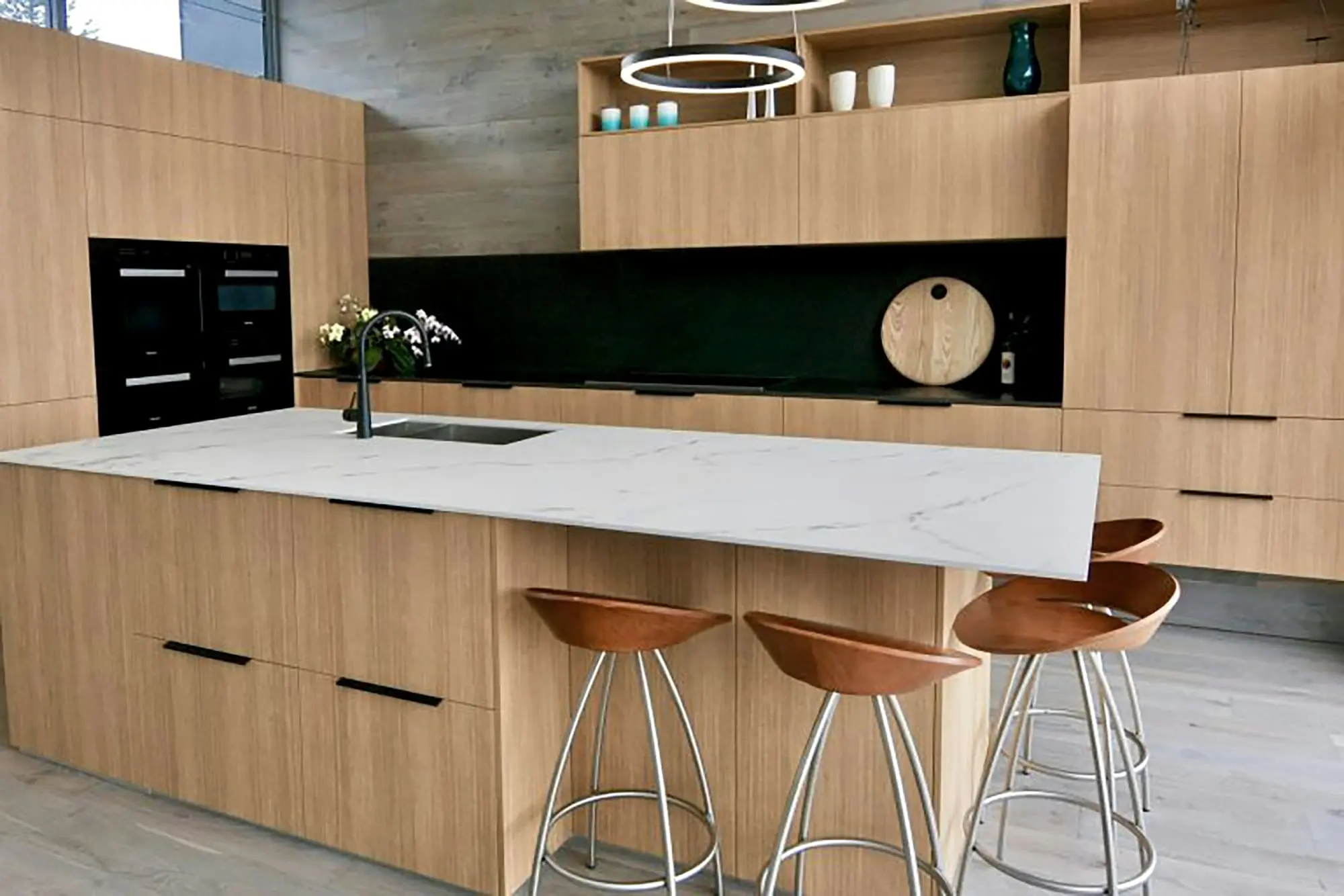 Oak kitchen with a marble island, copper stools and a dark green splashback