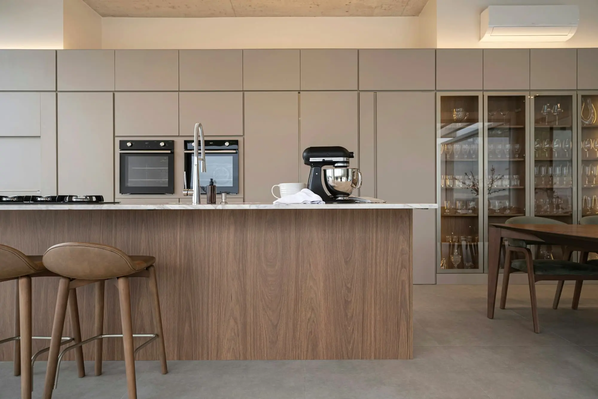 Kitchen with a walnut-fronted island, tall pale cabinets and a glazed display cabinet