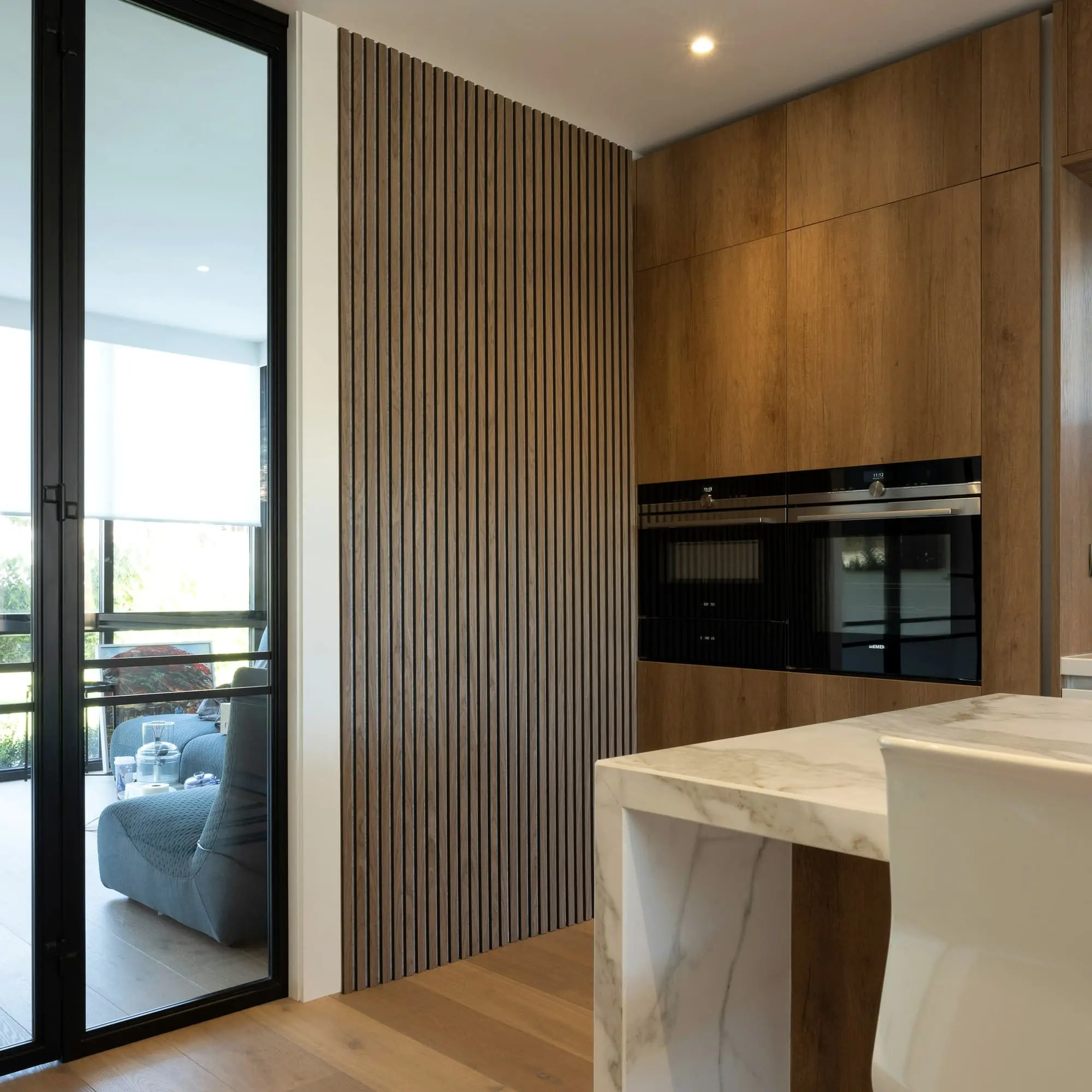 Oak slatted kitchen wall with integrated ovens and a marble worktop