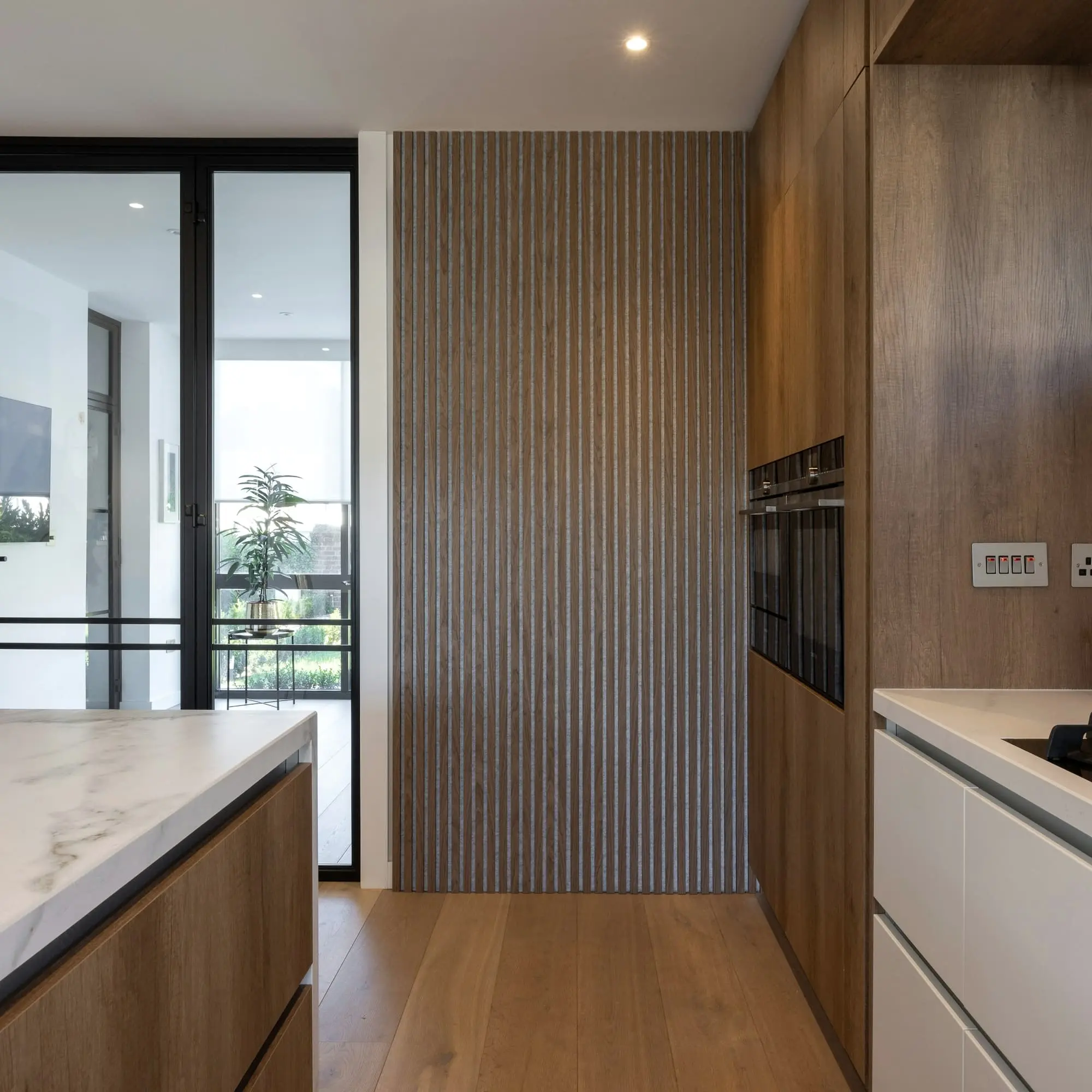 Fluted oak cabinetry with built-in ovens beside a glass door