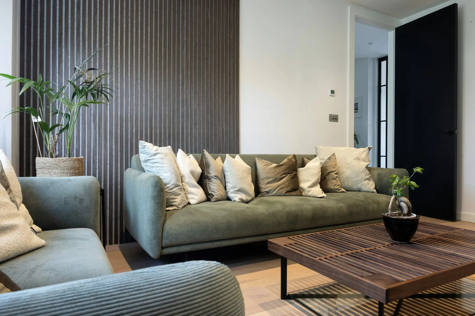 Living room with a walnut coffee table, green sofa and an oak slatted wall