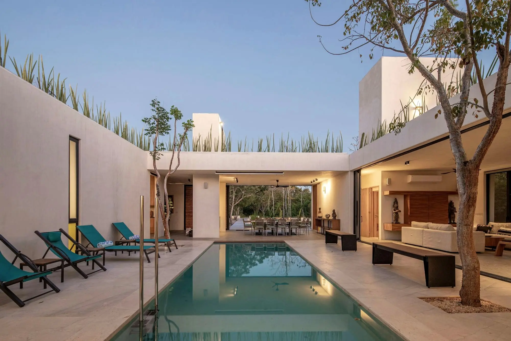 Courtyard pool with teal loungers, framed by pale walls and a covered living area